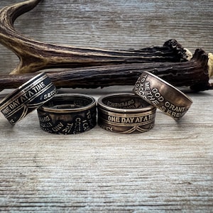 Può includere: Quattro anelli d'argento con testo inciso. Il testo sugli anelli recita "One Day at a Time", "God Grant Me the Serenity", "To Accept the Difference", e "One Day at a Time".
