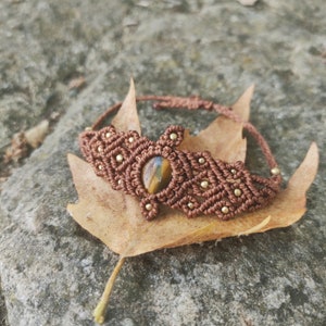May include: A brown macrame bracelet with a tiger's eye gemstone and gold beads.