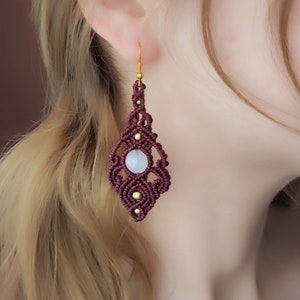 May include: Burgundy macrame earrings with a white gemstone and gold accents.