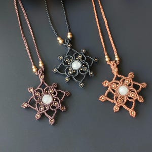 May include: Three macrame necklaces with a white stone pendant. The necklaces are made with brown, black, and copper cord. Each pendant is a starburst design with a white stone in the centre.