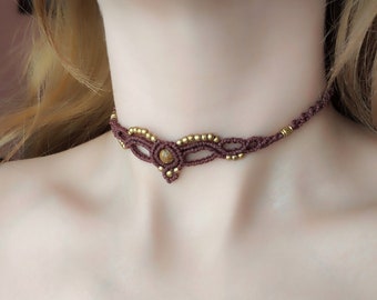 May include: A brown macrame choker necklace with a gold bead accent and a brown stone in the centre.
