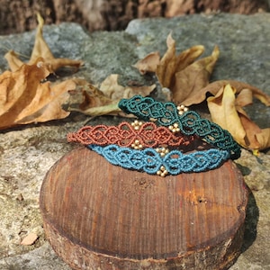 May include: Three braided bracelets with gold beads. The bracelets are teal, brown, and blue. The bracelets are stacked on a wooden surface.