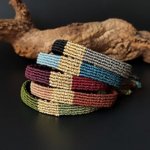 Peut inclure: Plusieurs bracelets d'amitié faits à la main, empilés les uns sur les autres. Les bracelets sont de couleurs variées : noir, bleu, gris, bordeaux et vert. Chaque bracelet est orné d'un détail doré.