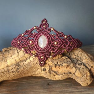 Può includere: Corona in macramè bordeaux fatta a mano, con una pietra ovale rosa pallido al centro. La corona è decorata con piccole perline dorate. Un accessorio in stile bohémien.