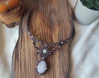 May include: A brown macrame necklace with a light pink and clear gemstone pendant. The necklace is decorated with gold beads.