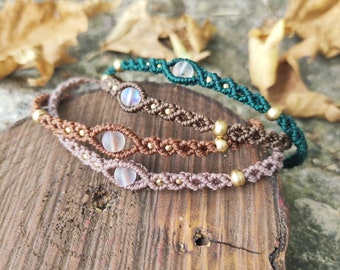 Könnte beinhalten: Drei geflochtene Armbänder mit schillernden Perlen und goldenen Akzenten. Die Armbänder liegen übereinander auf einer Holzoberfläche.