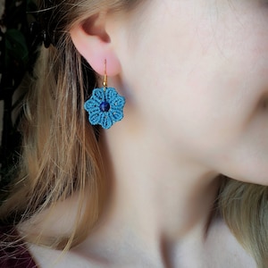 May include: Blue flower-shaped earrings with a dark blue gemstone in the centre. The earrings are made with macrame and have gold hooks.