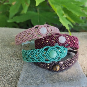 Könnte beinhalten: Vier geflochtene Armbänder mit verschiedenen Schnüren und Edelsteinperlen. Die Armbänder sind übereinander gestapelt. Das obere Armband ist rosa mit einem weißen Edelstein, das zweite Armband ist burgunderrot mit einem weißen Edelstein, das dritte Armband ist türkis mit einem grünen Edelstein und das untere Armband ist braun mit einem Tigerauge-Edelstein.