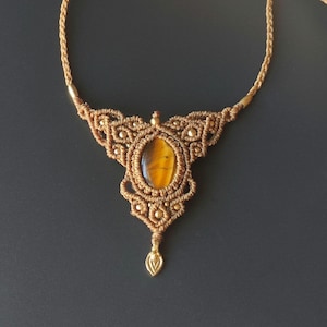 May include: A brown macrame necklace with a gold-toned pendant and a tiger's eye gemstone.