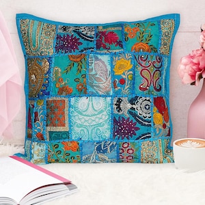 Puede incluir: Una funda de cojín de patchwork azul con bordados florales coloridos y lentejuelas. La funda de cojín está hecha de diferentes telas y tiene una forma cuadrada.