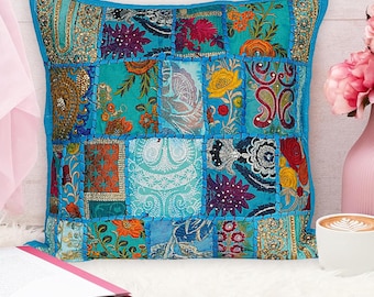 Puede incluir: Una funda de cojín de patchwork azul con bordados florales coloridos y lentejuelas. La funda de cojín está hecha de diferentes telas y tiene una forma cuadrada.