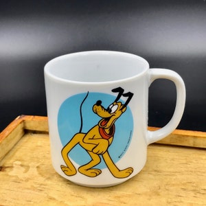May include: White ceramic mug with a blue circle and a cartoon image of Pluto the dog. The text "© WALT DISNEY PRODUCTIONS" is printed on the mug.