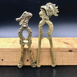 May include: A set of two antique brass nutcrackers, each shaped like a bird. The nutcrackers are detailed with intricate carvings and have a gold finish.