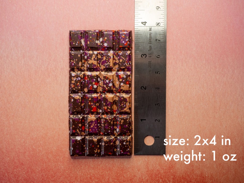 May include: A dark chocolate bar with a speckled pattern of purple, red, and gold. The bar is 2 inches by 4 inches and weighs 1 ounce.  size: 2x4 in weight: 1 oz