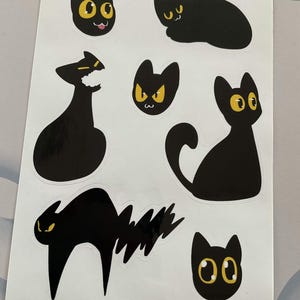 May include: A sheet of black cat stickers with yellow eyes. The stickers depict various cat poses, including sitting, lying down, and a cat with an open mouth. The stickers are on a white background.