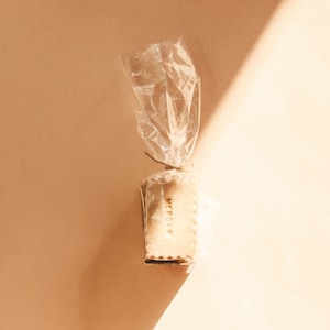 Pode incluir: Um único biscoito embrulhado em plástico transparente com um cordão marrom amarrado ao redor. O biscoito é retangular e tem a palavra "Merci" escrita nele.