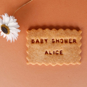 May include: A light brown sugar cookie with the text "BABY SHOWER ALICE" in white.
