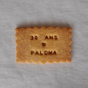 Op de afbeelding: Een lichtbruine koek met de tekst "30 ANS PALOMA" en een hartje.