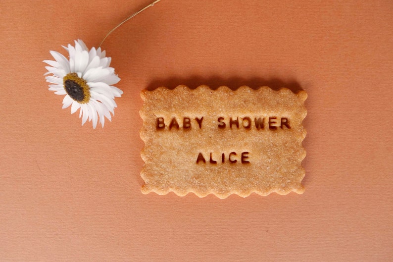 May include: A light brown sugar cookie with the text "BABY SHOWER ALICE" in white.