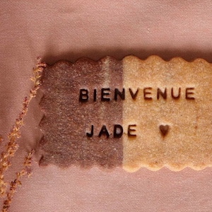 May include: A brown and beige cookie with the words "Bienvenue Jade" and a heart symbol.
