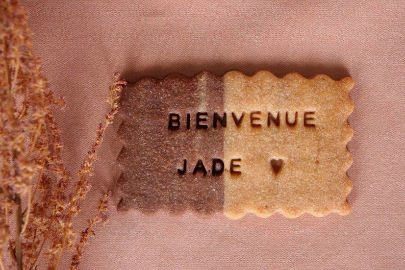 May include: A brown and beige cookie with the words "Bienvenue Jade" and a heart symbol.