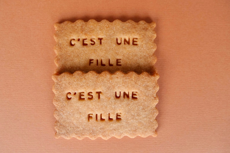 May include: Two brown sugar cookies with the text "C'est une fille" on each cookie.
