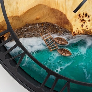 May include: A unique wall clock featuring a beach scene with a wooden pier, two small boats, and a turquoise ocean. The clock face is made of wood and resin, with a black frame. The clock hands are black.