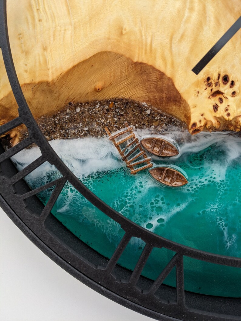 May include: A unique wall clock featuring a beach scene with a wooden pier, two small boats, and a turquoise ocean. The clock face is made of wood and resin, with a black frame. The clock hands are black.
