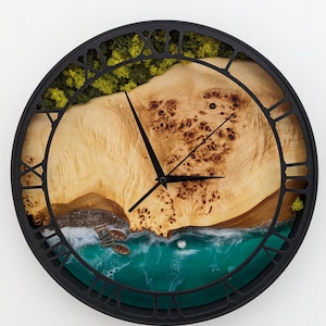 Könnte beinhalten: Eine runde Wanduhr mit schwarzem Rahmen und römischen Ziffern. Das Zifferblatt zeigt ein natürliches Holzmaserungsmuster mit einem türkisfarbenen Harzmeer und kleinen Booten. Grünes Moos und eine Holzlandschaft sind ebenfalls sichtbar.