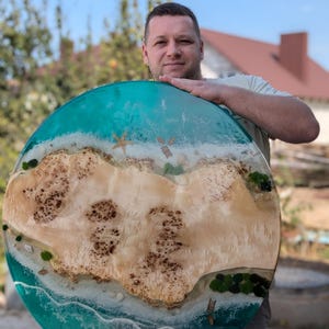 May include: A round, turquoise resin table top with a white sandy beach and a small island in the center. The island is made of wood and has a brown, natural wood grain. The table top is approximately 30 inches in diameter.