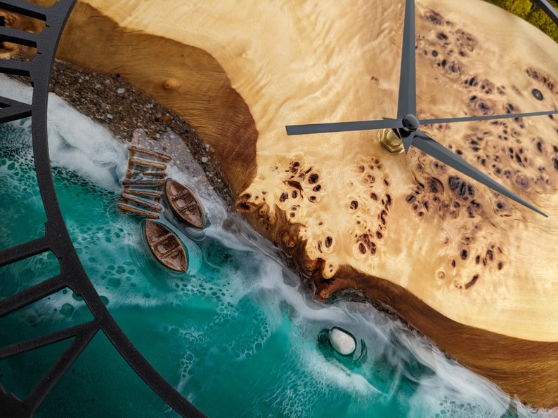 May include: A unique wall clock featuring a beach scene with a wooden dock and two small boats. The clock face is made of wood and resin, with black clock hands and a black metal frame. The clock measures approximately 12 inches in diameter.