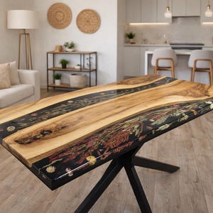 Op de afbeelding: Een handgemaakte houten tafel met een zwart epoxyhars en gedroogd bloemendesign. De tafel heeft een natuurlijk houten blad en een zwart metalen onderstel. De tafel is een uniek meubelstuk voor een woon- of eetkamer. De tafel is ongeveer 150 cm lang.