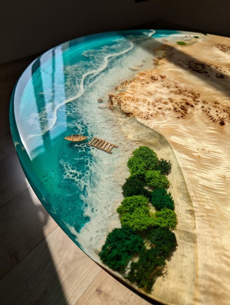 May include: A round, turquoise resin table top with a miniature beach scene. The scene includes a sandy beach, a small boat, a wooden dock, and green moss trees.