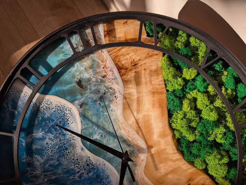 Pu&ograve; includere: Un orologio da parete rotondo con una cornice in metallo nero. Il quadrante presenta un design oceanico blu e bianco, una sezione in legno e una sezione di muschio verde. Le lancette dell'orologio sono nere.