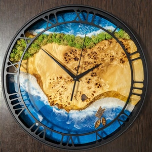 May include: A round wall clock with a black frame and Roman numeral markings. The clock face features a resin art design of a beach scene with blue water, white sand, and green moss.
