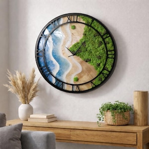 May include: A large, round wall clock with a black metal frame and Roman numerals. The clock face features a beach scene with blue water, sandy shores, and green foliage. The clock hands are black.