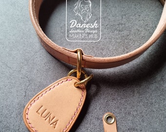May include: A light brown leather dog collar with a gold metal D-ring and a matching leather tag that says "LUNA" in pink stitching.