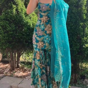 May include: A teal floral print dress with spaghetti straps and a matching teal scarf. The dress features a variety of floral patterns in shades of brown, blue, and teal. The scarf has a delicate embroidered design.