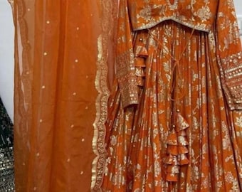 Può includere: Un abito ricamato in arancio e oro con un dupatta abbinato. L'abito ha una scollatura a V profonda e maniche lunghe. Il dupatta è trasparente e ha un bordo dorato.