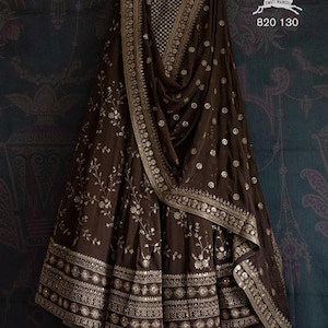 Puede incluir: Una falda y un dupatta a juego de color marrón y dorado bordados con intrincados motivos florales y un borde dorado. La tela es transparente y tiene una textura delicada. La falda tiene una silueta acampanada y el dupatta está drapeado sobre el hombro. El texto "820 130" es visible en la esquina superior derecha de la imagen.