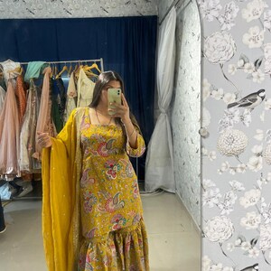 Peut inclure: Ensemble salwar kameez jaune moutarde avec un col carr&eacute; et un imprim&eacute; cachemire. La tenue comprend un dupatta assorti et un ourlet &agrave; volants. Le tissu a un &eacute;clat subtil, et le motif incorpore des accents roses, bleus et verts.