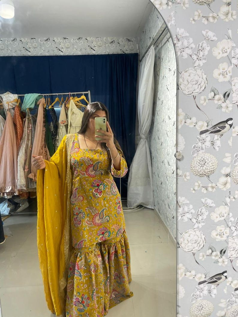 Peut inclure: Ensemble salwar kameez jaune moutarde avec un col carr&eacute; et un imprim&eacute; cachemire. La tenue comprend un dupatta assorti et un ourlet &agrave; volants. Le tissu a un &eacute;clat subtil, et le motif incorpore des accents roses, bleus et verts.
