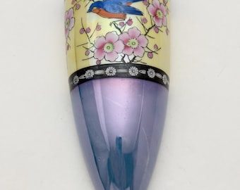 May include: A wall pocket vase with a pointed base, featuring a central band of pale yellow decorated with a blue bird and pink flowers. The top and bottom sections are finished in a glossy, iridescent purple glaze, framed by black borders with white floral patterns.