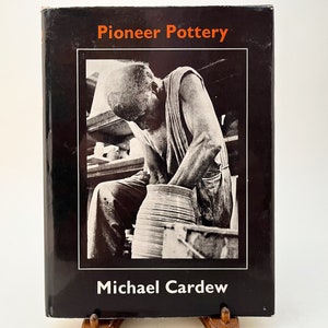 May include: Black and white photo of a book cover featuring a person making pottery on a pottery wheel. The book title is "Pioneer Pottery" and the author is "Michael Cardew".