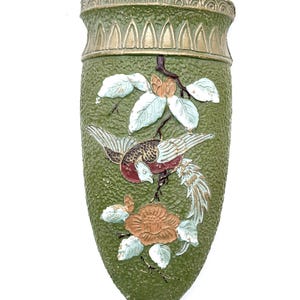 May include: A wall pocket planter featuring a textured olive green finish with a gold-toned rim. The front displays a raised relief design of a bird perched on a branch with a large flower, accented in shades of white, brown, and metallic gold.