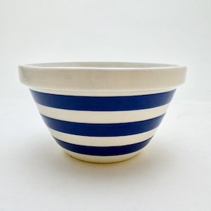 May include: A ceramic mixing bowl with a cream-colored rim and alternating horizontal stripes of navy blue and white. The bowl has a rounded shape and is suitable for kitchen use.