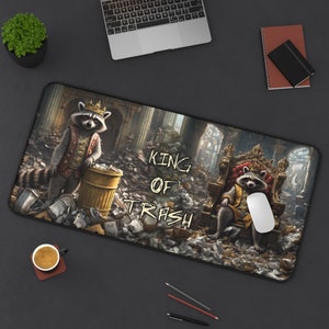 May include: A black and grey mouse mat featuring a cartoon raccoon wearing a crown and holding a bin. The text "KING OF TRASH" is printed on the mouse mat.