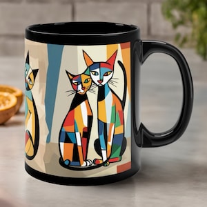 May include: Black coffee mug with a colorful abstract design of three cats. The cats are stylized with geometric shapes and bright colors, including red, yellow, blue, green, and orange.