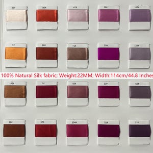 Peut inclure: Un nuancier composé de trente petits échantillons rectangulaires de tissu en soie 100 % naturelle dans diverses nuances de rose, rouge, violet et marron. Chaque échantillon est numéroté. Le texte indique : 100% Natural Silk fabric; Weight:22MM; Width:114cm/44.8 Inches.