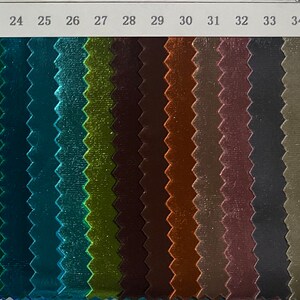 May include: A colour swatch card featuring samples of shiny fabric in various colours. The samples are arranged in vertical rows, showcasing shades of blue, green, brown, and gold. The numbers 19 to 35 are printed at the top.